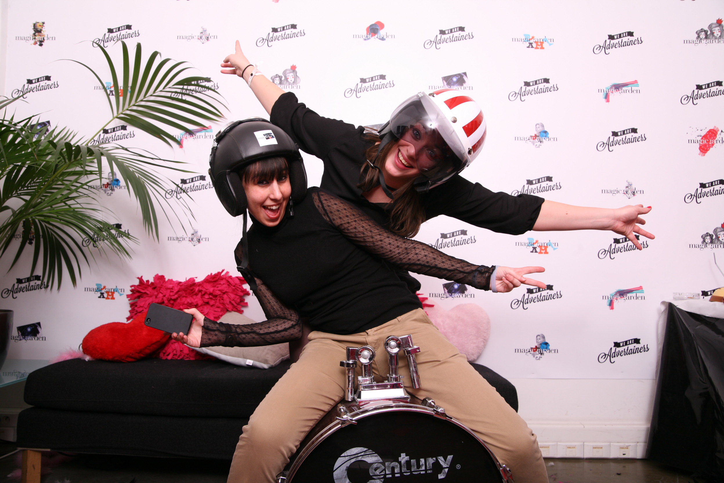 Photo prise dans un Photocall de deux femmes assises sur une grosse caisse et déguisées d'un casque de moto devant un fond de type photocall